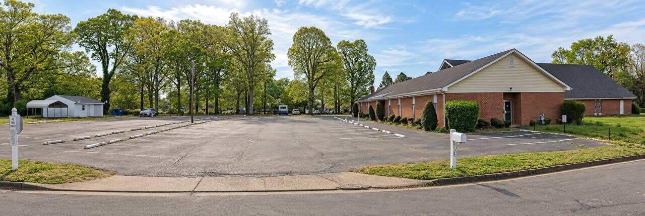 Wide view of the church parking lot at 2210 Carter St, Richmond, VA, lined with trees, next to the brick church building